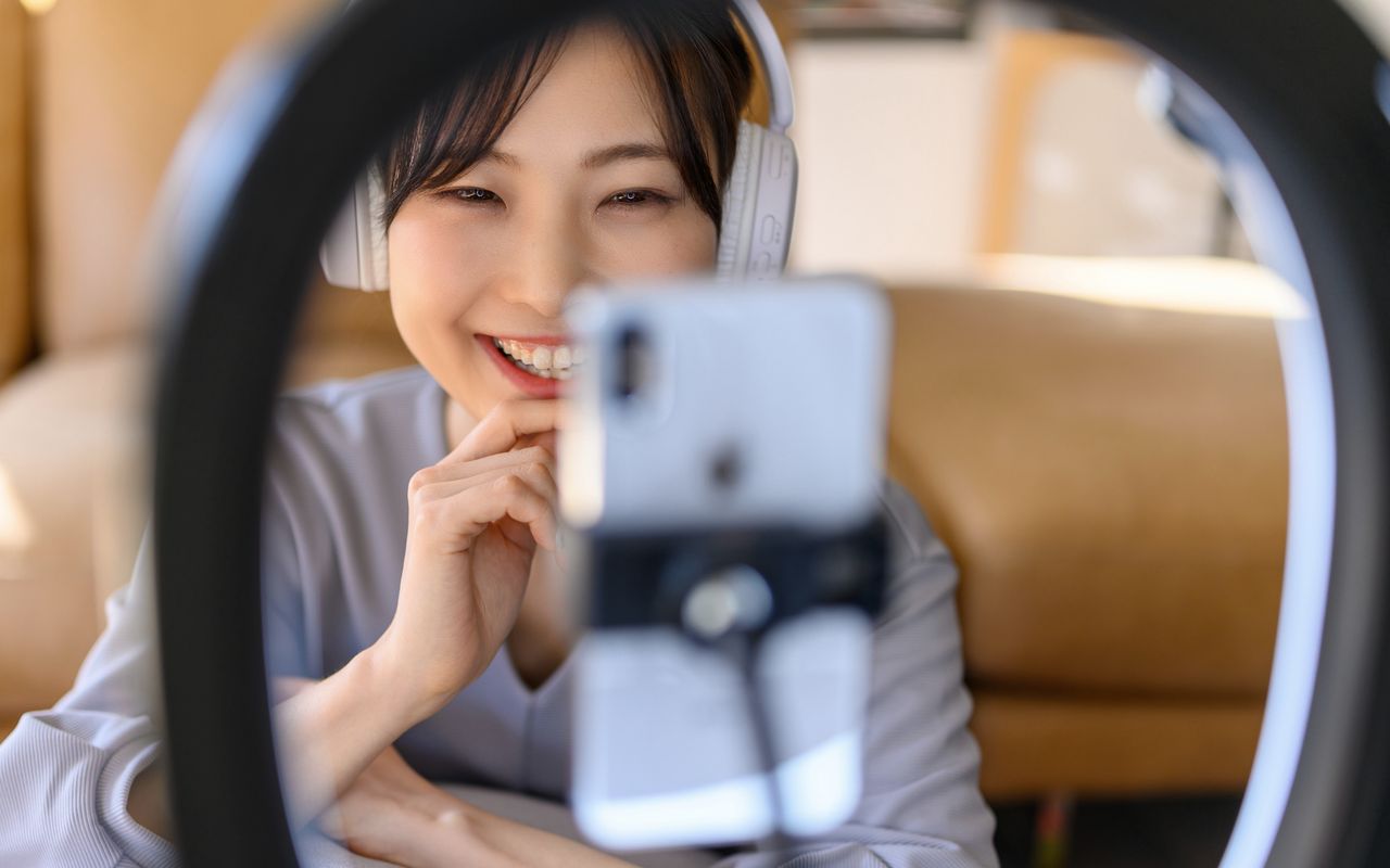 リングライト越しにスマートフォンでライブ配信する女性